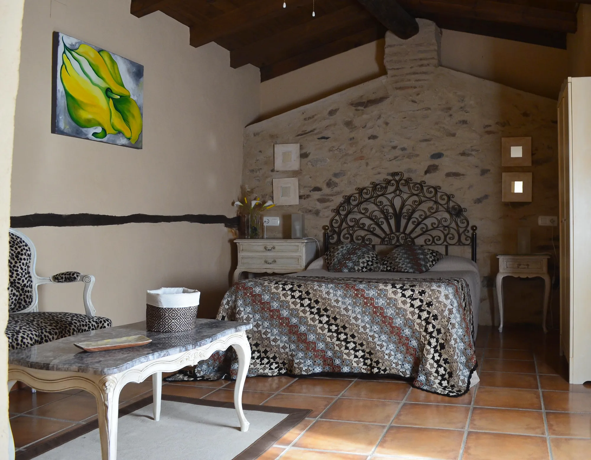 Habitación de matrimonio con cabecero de forja y muro de piedra